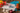 Fotografía cuchillo de verduras 130 mm serie Brooklyn en una tabla de corte de mármol con distintas verduras como cebollas, tomates, pimientos rojos, verdes y amarillos, y chambiñones.